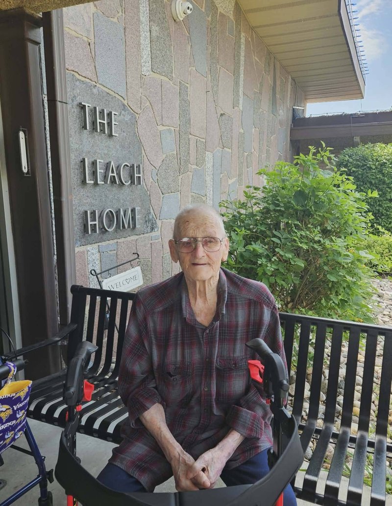 A resident enjoying the sunshine by The Leach Home sign at our front entrance