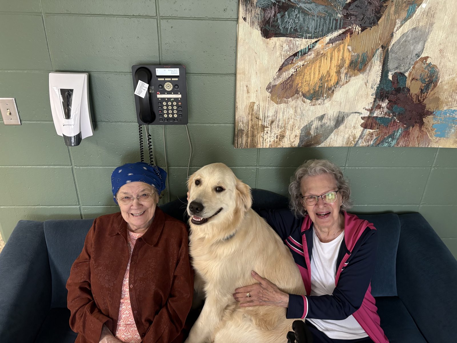 Two residents smiling with a golden retriever between them